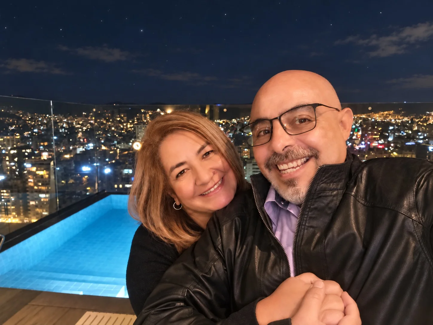 Frank y Nel abrazados en una terraza de noche, con las luces de la ciudad al fondo